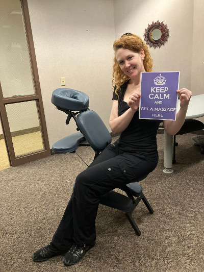 At a corporate massage event in the Twin Cities Lorie holds a sign that reads: Keep Calm and Get a Massage Here!